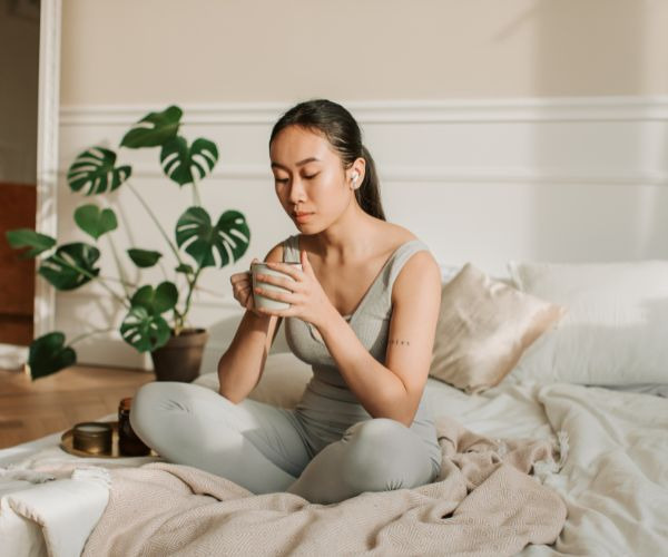 a woman sitting on a bed with a cup of coffee