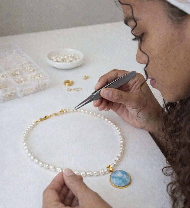 Joyero que utiliza pinzas para armar un collar de perlas blancas con un colgante de Larimar.