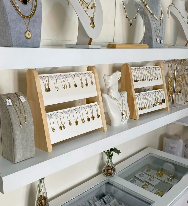 Elegante exhibición boutique con collares de oro y joyas de perlas en estantes y bustos blancos.