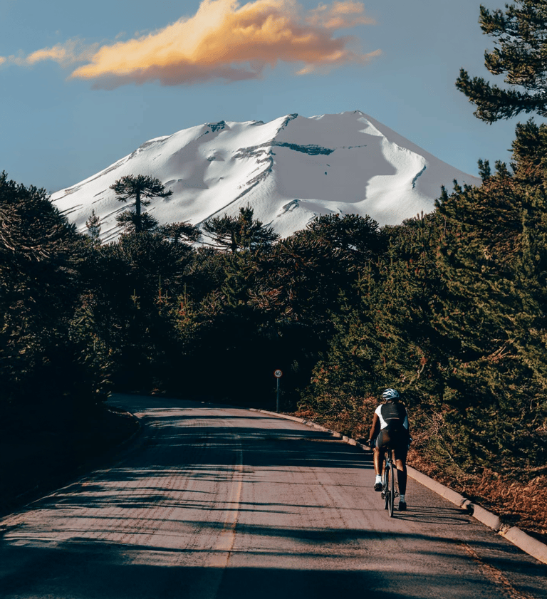 Ciclista recorriendo ruta escénica pavimentada en Lonquimay con vista al Volcán nevado y bosques de 