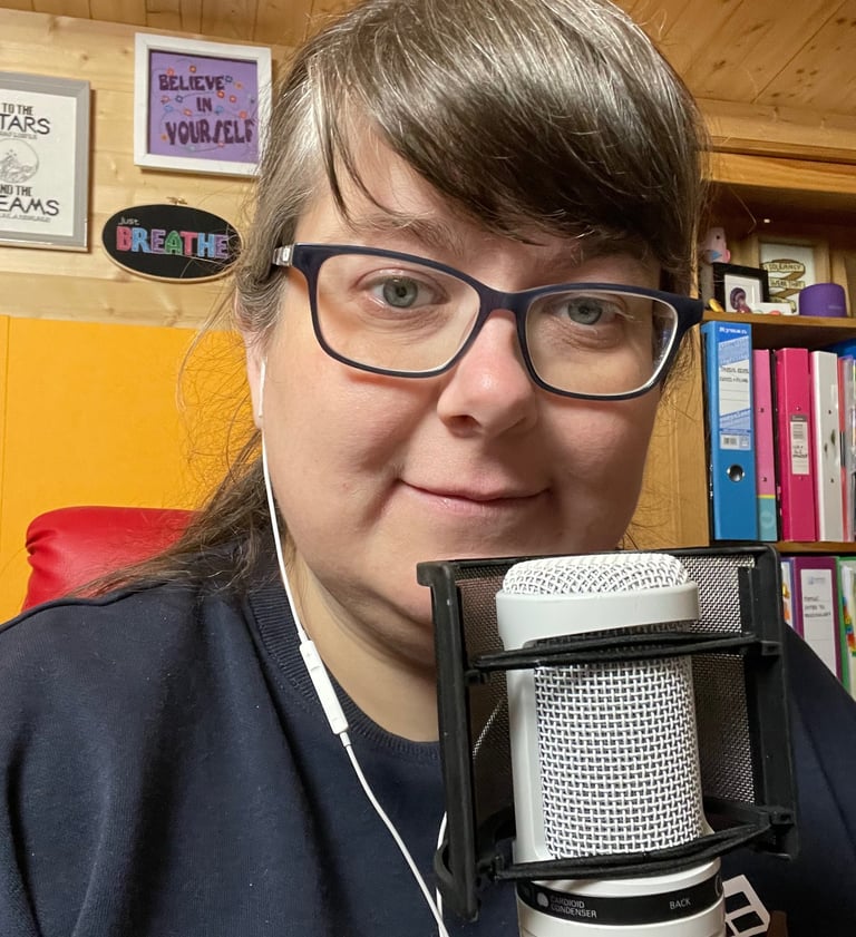 Laura Dumbleton at her recording setup with a microphone and BREATHE sign on the wall behind her
