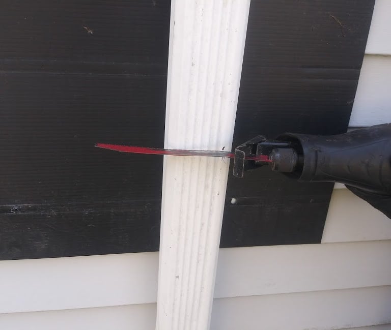 Using a saw to cut a downspout to install a rain barrel under it to collect rainwater 