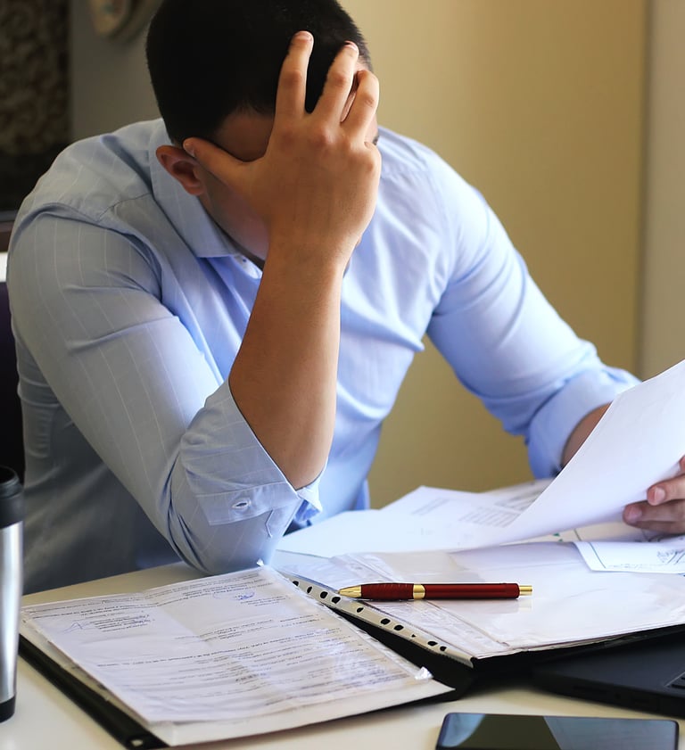 um homem em frente a papeis e com a mão no rosto em postura de preocupação