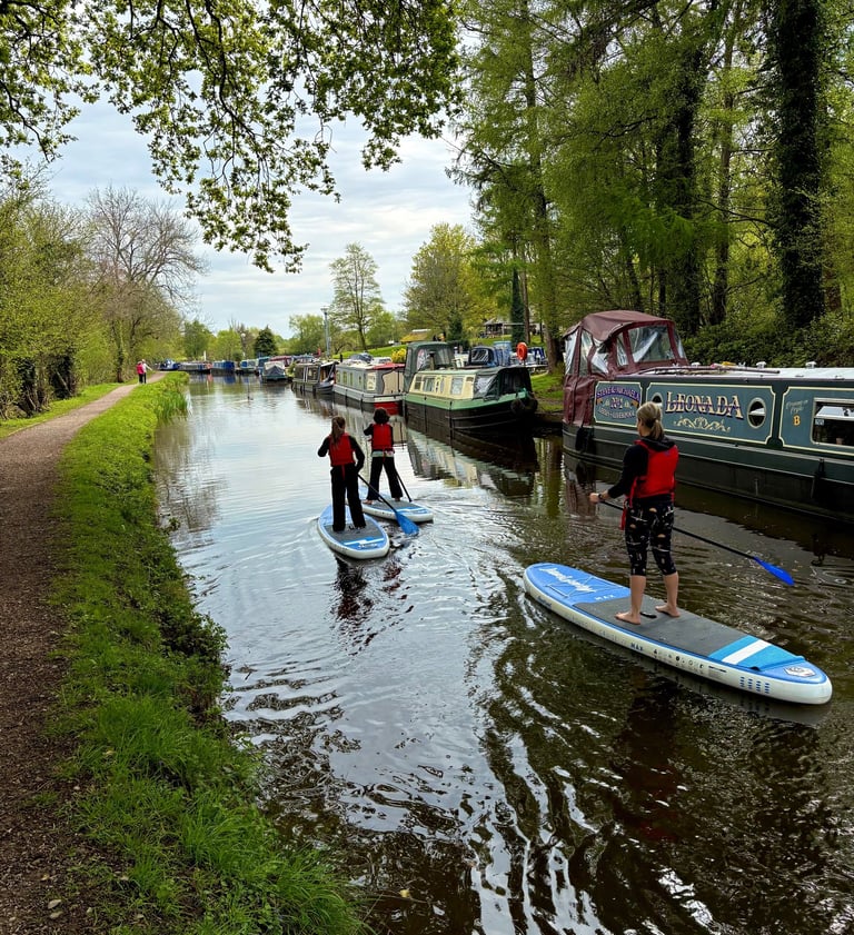 A family including two children paddle on the Monmouthshire and Brecon canal on SUP's hired from Bridge 76 Adventures.