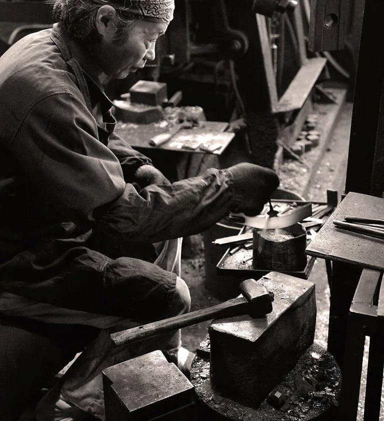 Historische Schwarzweißaufnahme eines japanischen Messerschmieds in einer traditionellen Schmiede in