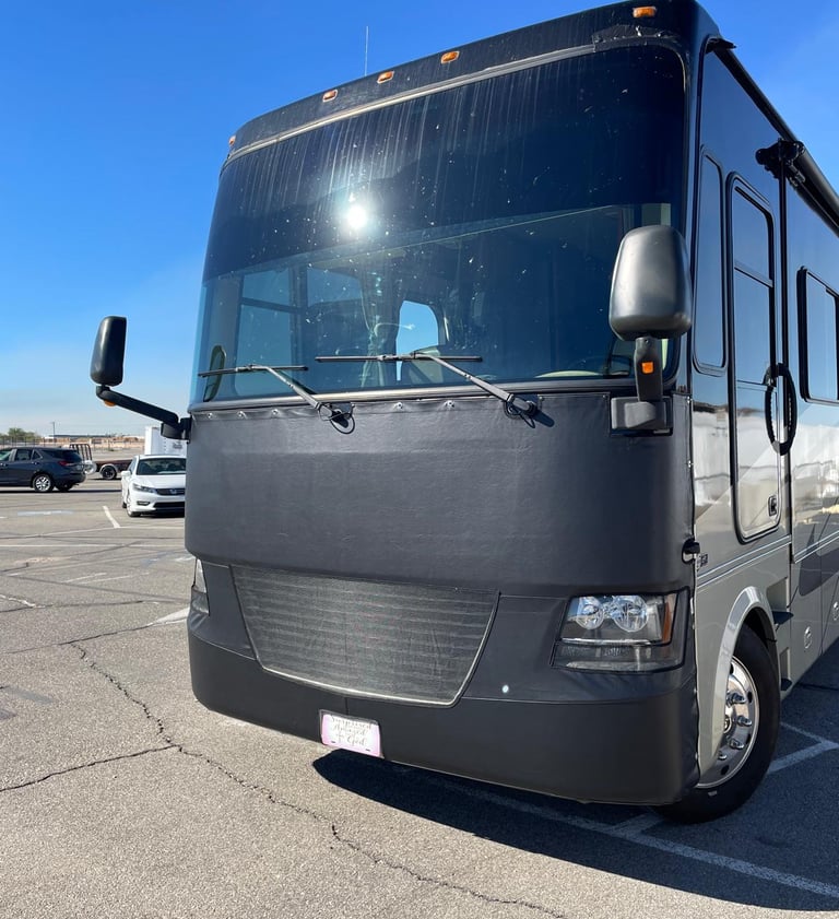 A black Class A motorhome with a protective vinyl bra cover parked in a sunny lot.