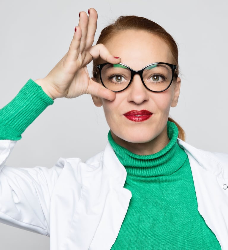 eine Therapeutin mit freundlichem Gesicht und Zopf fasst sich mit der rechten Hand an Ihre Brille ,