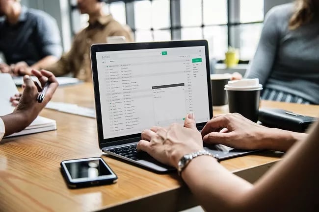 Vista em close de profissional redigindo e-mail em um notebook sobre mesa de madeira