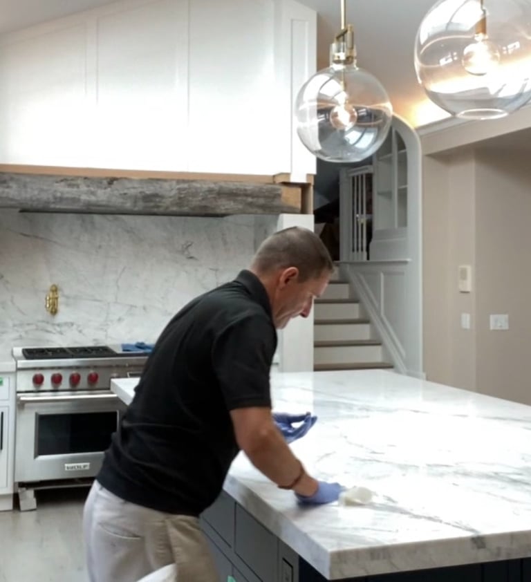 Professional contractor sealing a white marble kitchen island countertop during a home renovation.
