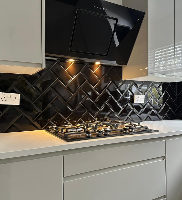Modern white kitchen featuring a black glass herringbone tile backsplash and gas stovetop.