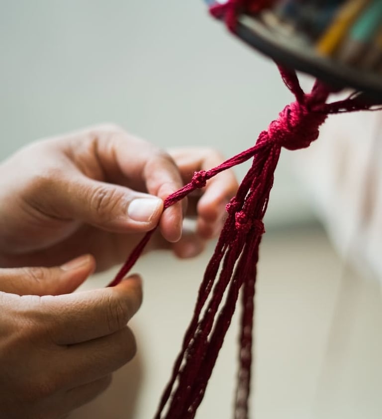 Manos atando cuidadosamente nudos en un cordón rojo para un proyecto artesanal o textil hecho a mano