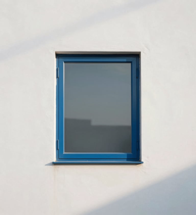 A minimalist architectural photograph of a single steel blue window frame against a soft cloud white wall. The composition is clean and centered, emphasizing the geometric purity and the soft play of morning shadows.
