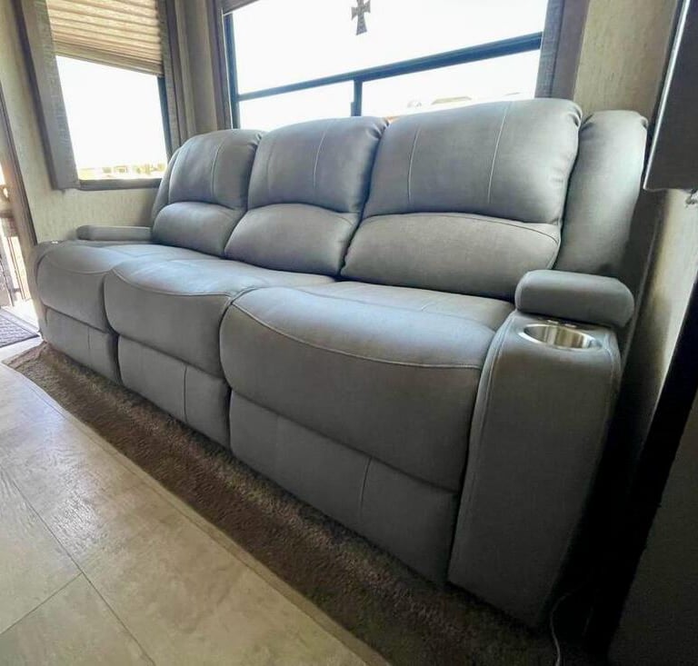 Modern gray leather power reclining sofa with integrated cup holders inside a motorhome living area.