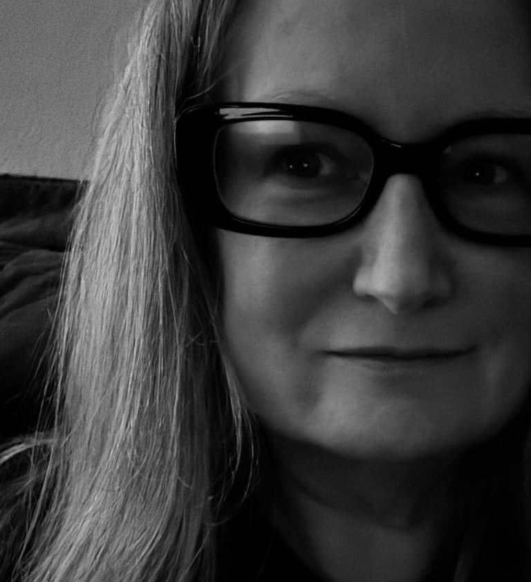A black and white close-up portrait of a woman with long hair wearing thick black framed glasses.