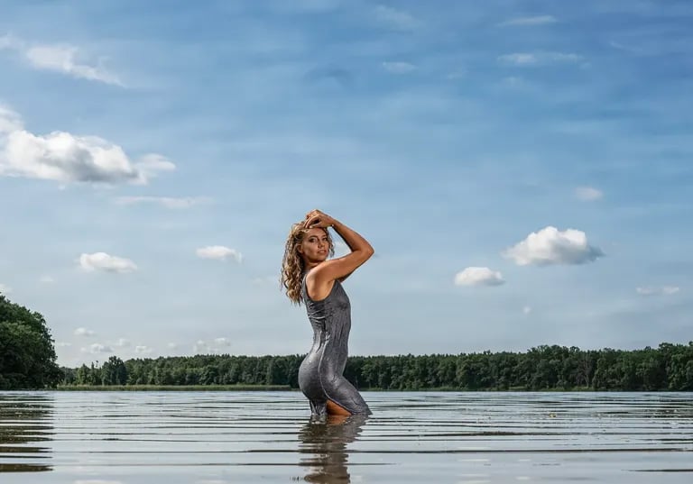 Porträt einer Frau in nassem Kleid, die kniehoch im Wasser eines Sees steht. 