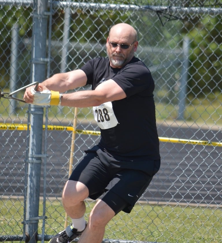 A male athlete wearing black athletic gear and sunglasses competes in a hammer throw event.