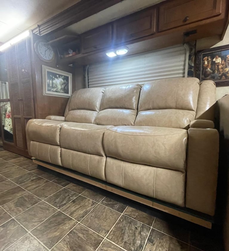 Tan leather reclining sofa in an RV living area with wood cabinets and tile flooring.