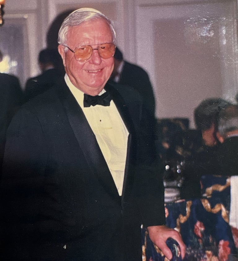 An older man in a suit smiling as he looks off to the left. 
