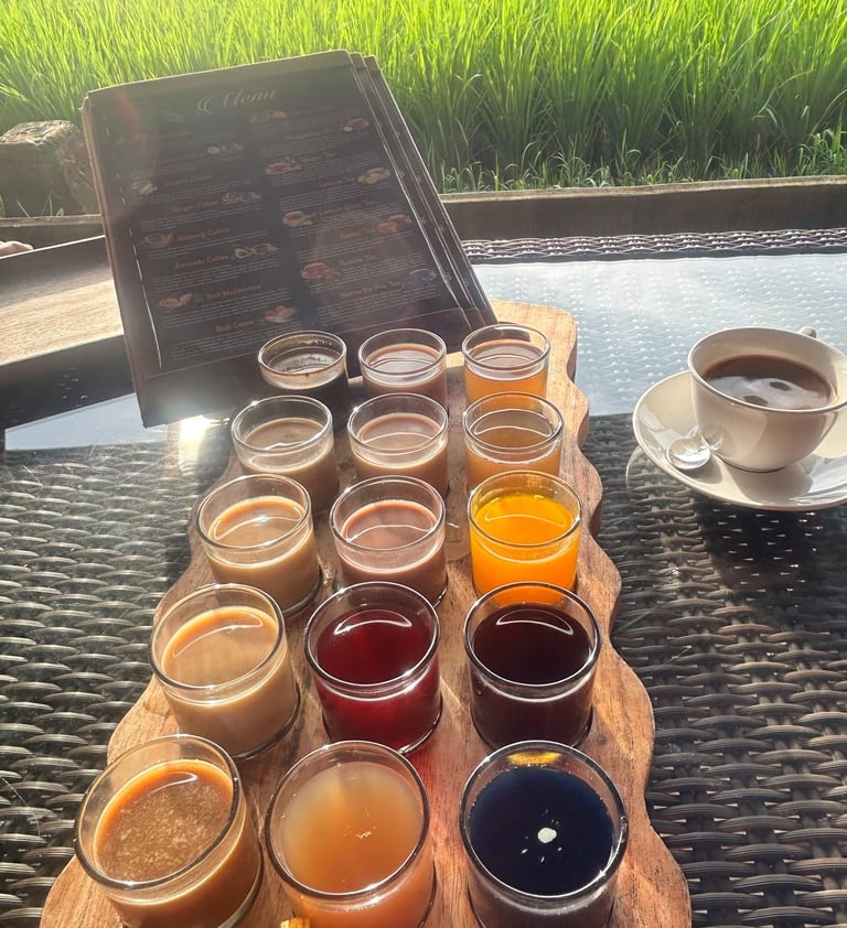 A colorful coffee and tea tasting flight on a wooden tray with a lush green rice field background in Bali.