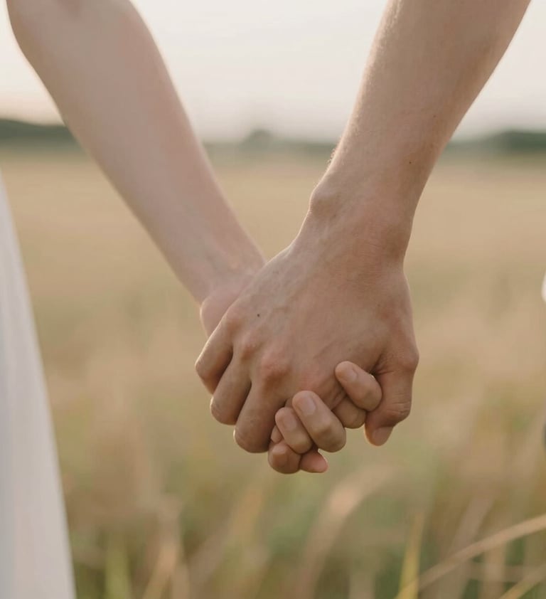 Macro shot of two people holding hands in a field, intimate and emotive. Soft focus background, warm #F8F4F0 skin tones and soft golden hour light.