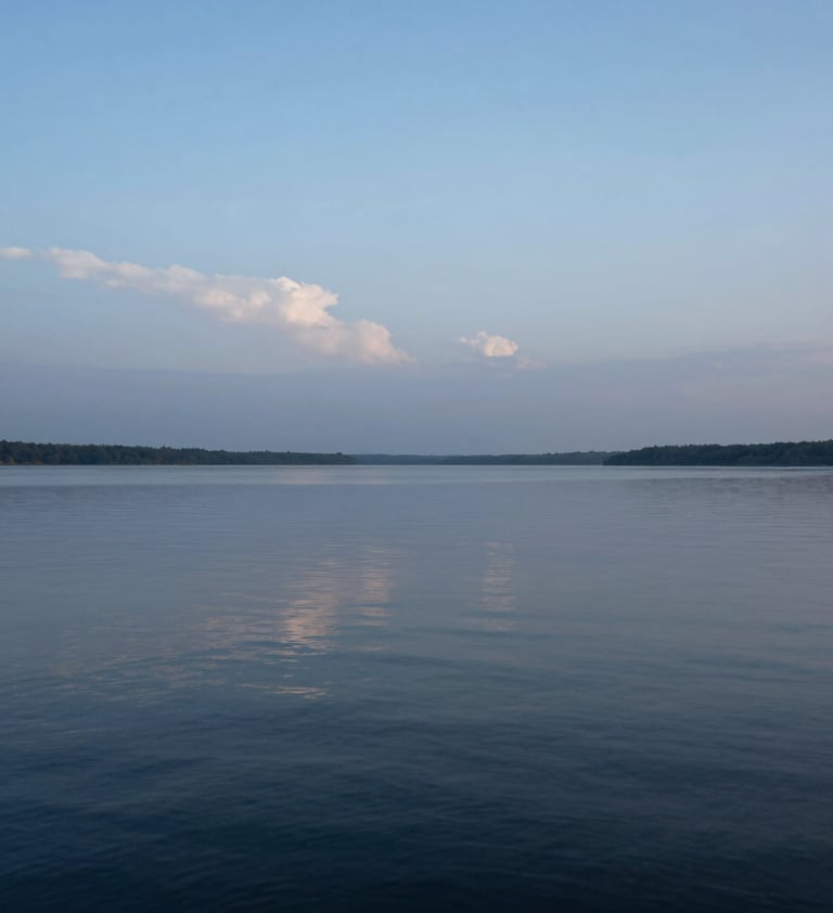 A high-resolution landscape photograph of a calm lake under a pale blue twilight sky. The water reflects the subtle light-grey clouds above. Minimalist and peaceful composition with professional lighting. International / Western nature scene.