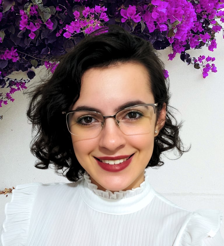 Smiling woman with short dark curls and glasses in front of purple flowers.