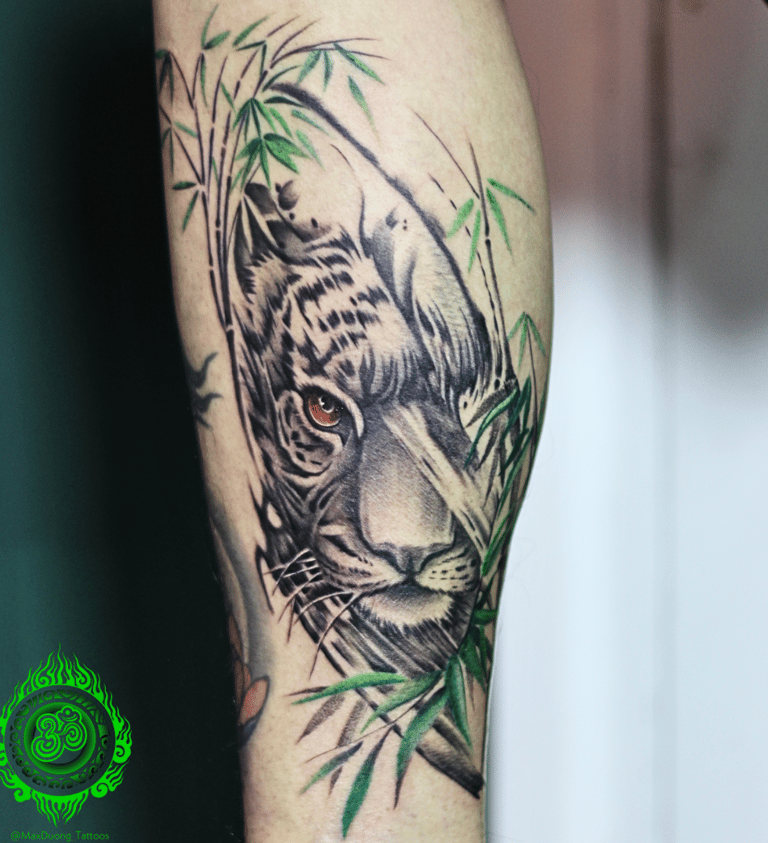 Realistic tattoo of a tiger with green bamboo on the calf