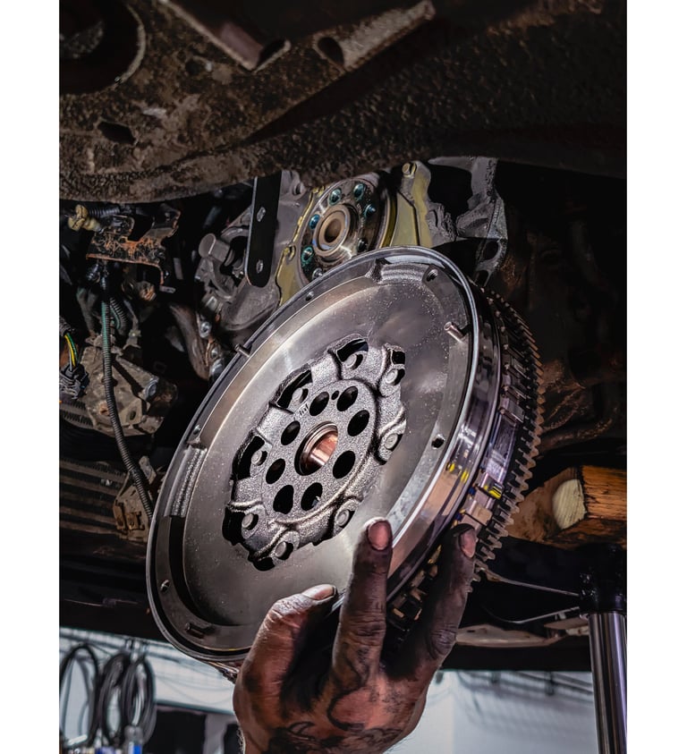 A mechanic installing a new dual-mass flywheel into a car engine during a clutch repair service.