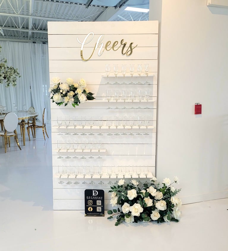 White champagne with white roses and greenery flowers and a sign that says cheers