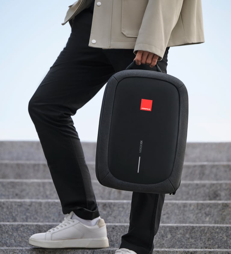 A man carrying a black XD Design anti-theft laptop bag while walking up stone stairs.