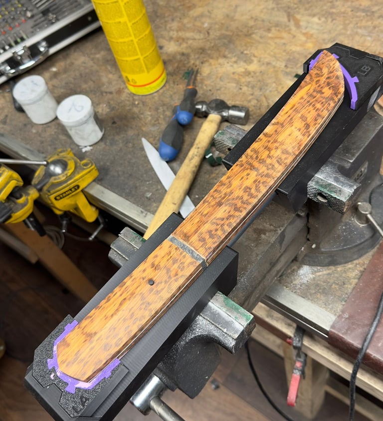 Wood grain knife handle clamped in a metal vice on a workshop workbench for crafting.