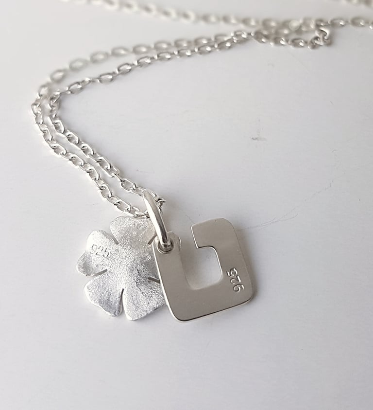 Sterling silver necklace with a four-leaf clover and square letter U charm, both stamped with 925 hallmarks.