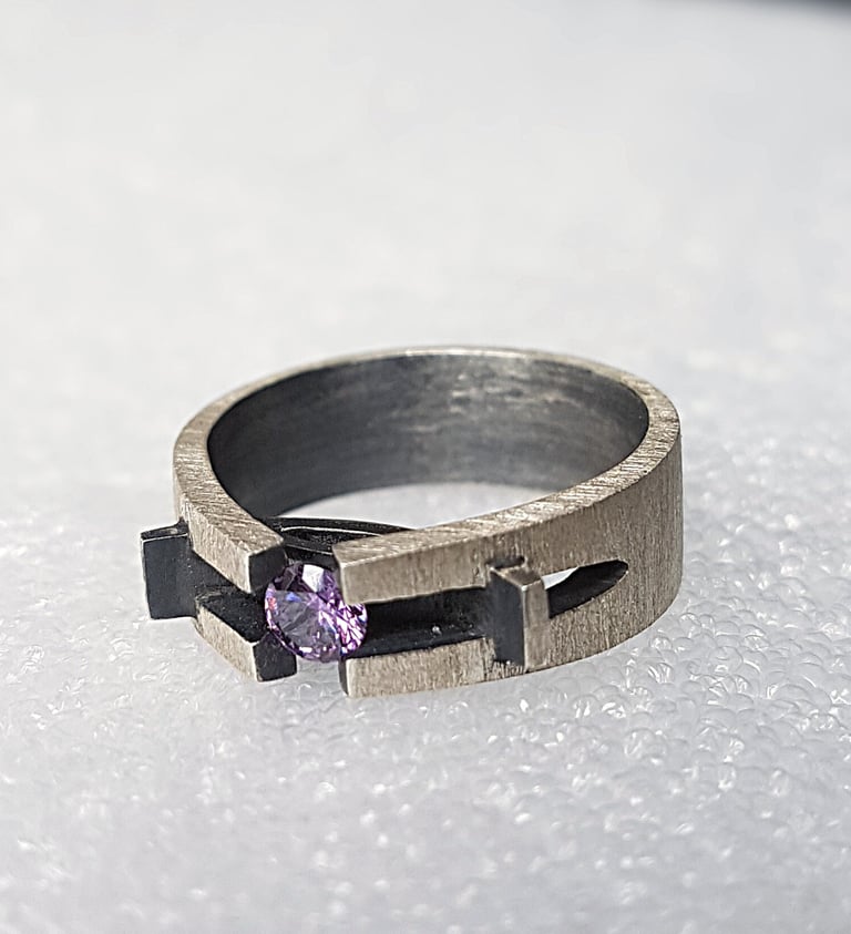 Handcrafted brushed silver ring featuring a round purple gemstone in a unique architectural setting.