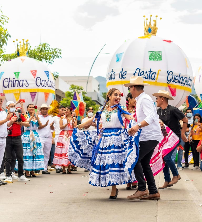Bailarines folclóricos oaxaqueños celebrando la Guelaguetza en la calle con marmotas y público