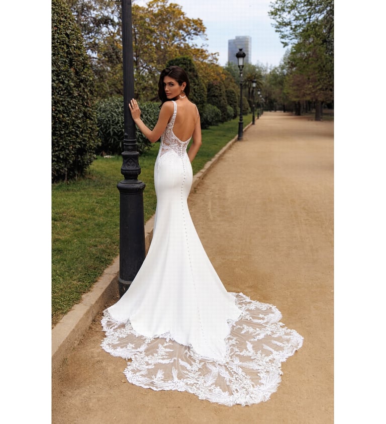 Elegant backless mermaid wedding dress with a long lace train on a park path.
