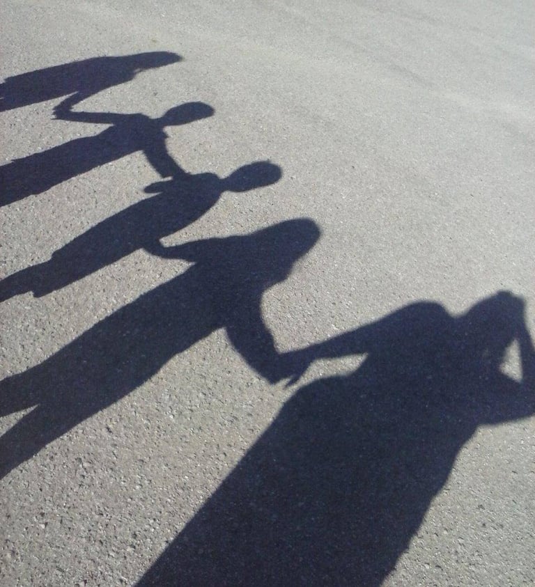 Shadows of a group of people holding hands on a gray pavement surface to represent unity and teamwork.