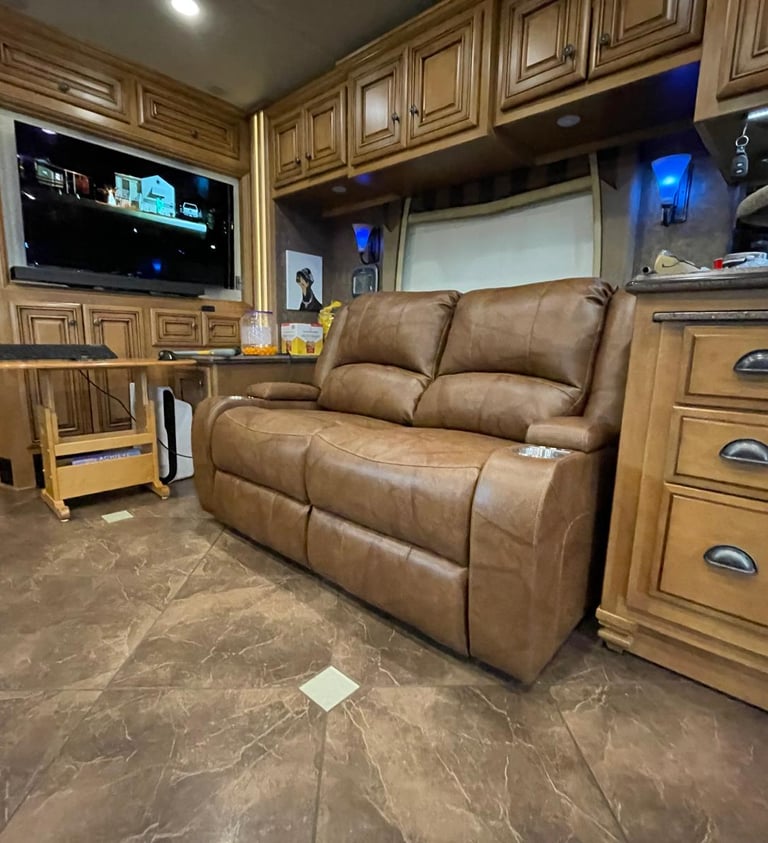 Luxury RV interior featuring a brown leather recliner sofa, wooden cabinets, and a flat-screen TV.
