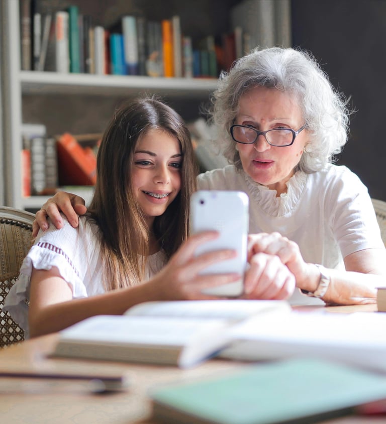 a woman and a young girl are sitting at a table looking at phone.