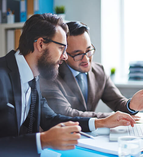 two men sitting at a desk with a laptop