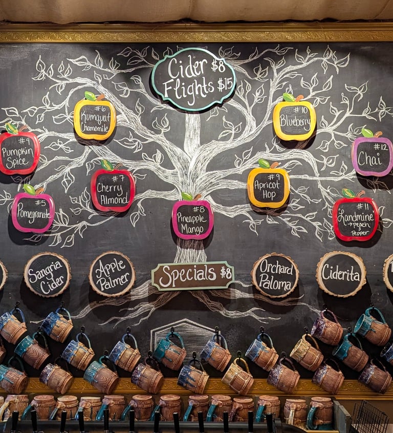 Hand-drawn chalkboard menu at a cidery displaying craft cider flavors, flight prices, and ceramic mugs.