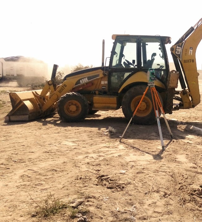 Yellow Cat backhoe loader and surveying equipment on a dusty construction site for land excavation.