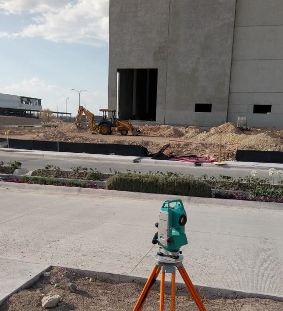 A digital total station on a tripod performing land surveying at a commercial building construction site.