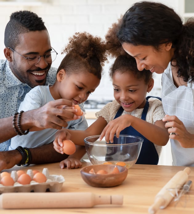 a family breaking eggs as they prepare food together