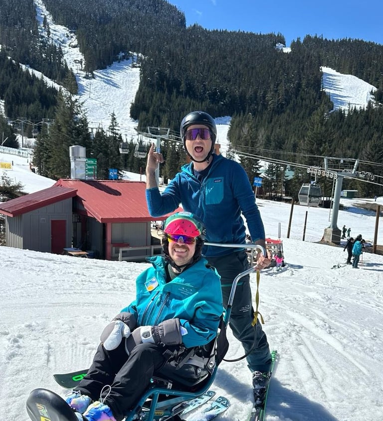 Sean in his sit ski with instructor Adria both wearing instructor jackets with big smiles on