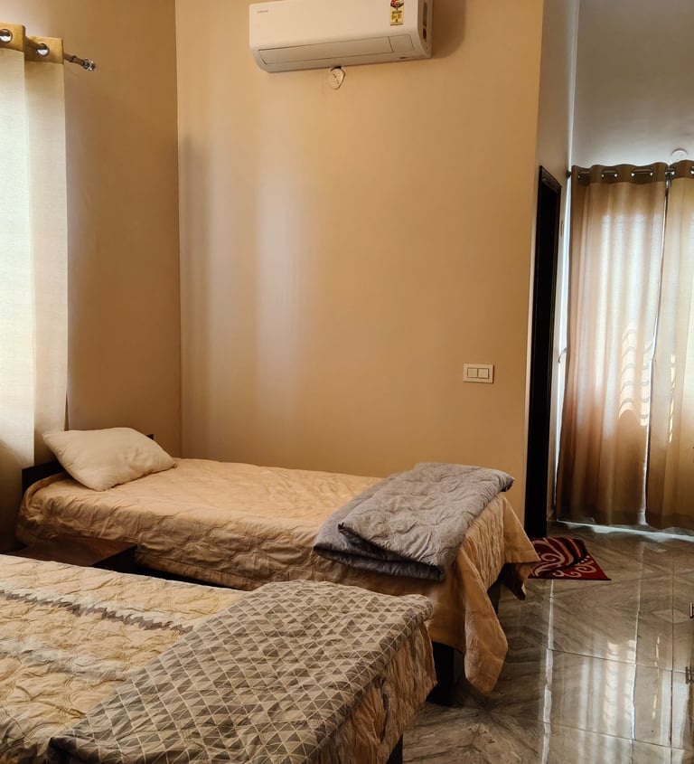 Cozy bedroom with twin beds, neutral curtains, and wall-mounted air conditioning unit for comfort.