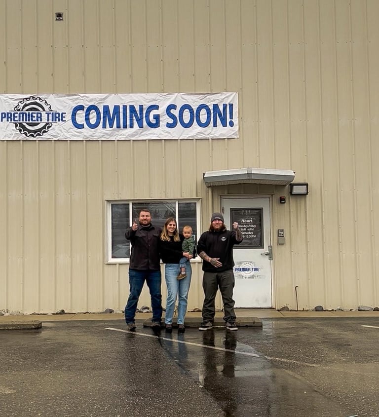 A family stands in front of the new Premier Tire shop with a coming soon banner displayed overhead.
