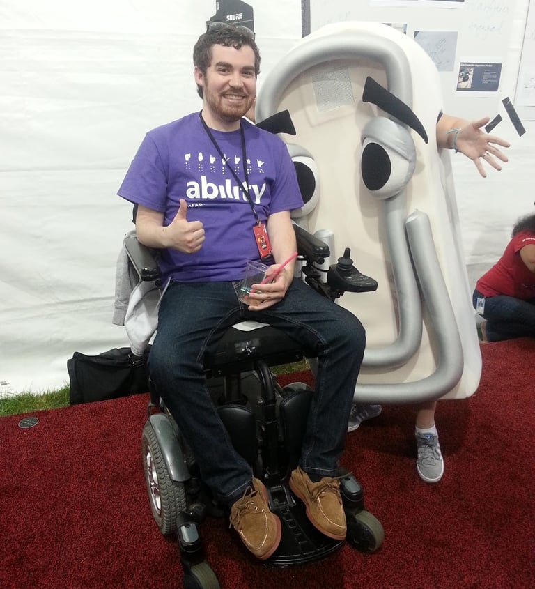 Sean in a purple "Ability" t shirt next to a life-size Microsoft Clippy costume