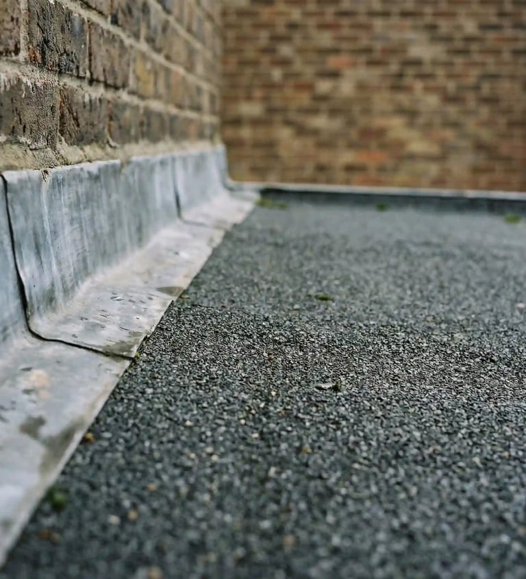 Close-up of lead flashing installation on a flat felt roof against a brick wall.
