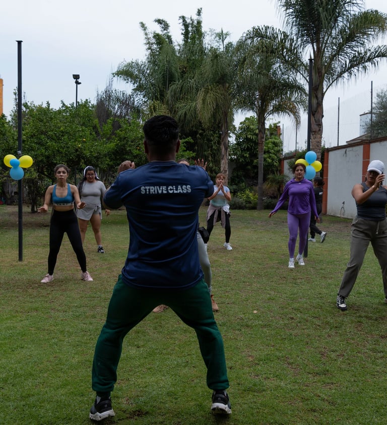 A group of diverse women participating in an outdoor Strive Class fitness session on a grassy lawn.