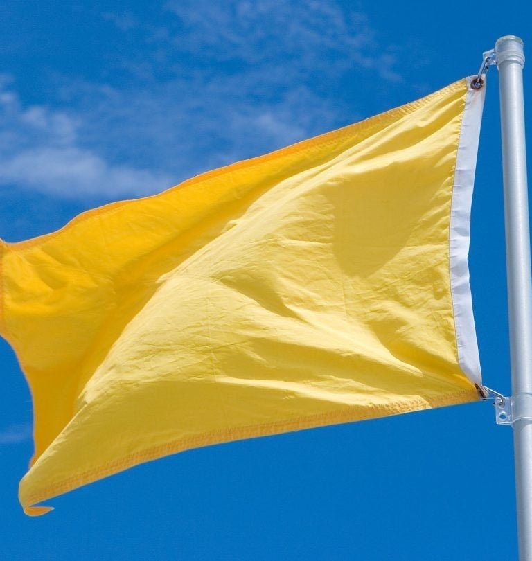 a yellow flag on a flagpoler in front of a blue sky
